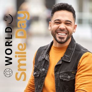 Man in yellow-orange sweatshirt smiling while walking. world smile day graphic.